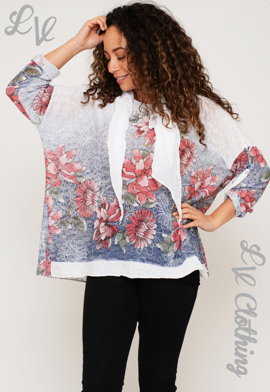 Floral print ladies top with draped white scarf and pink/red flowers on blue